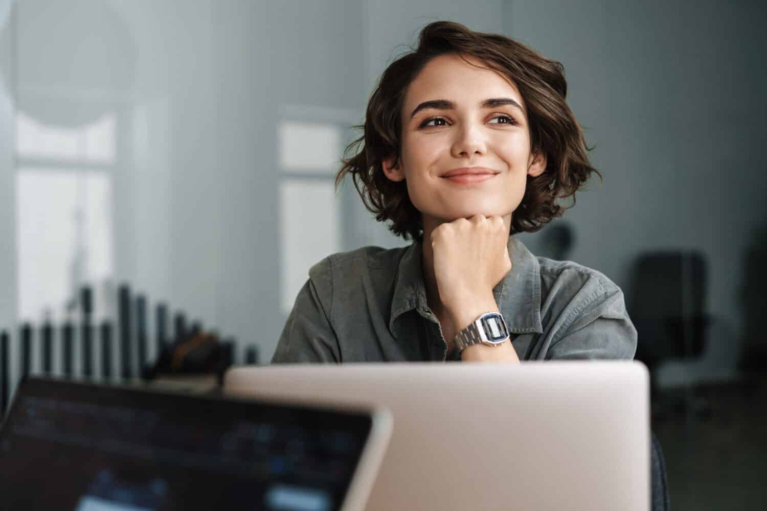 Immagine di giovane bella donna allegra che sorride mentre lavora con il portatile in ufficio