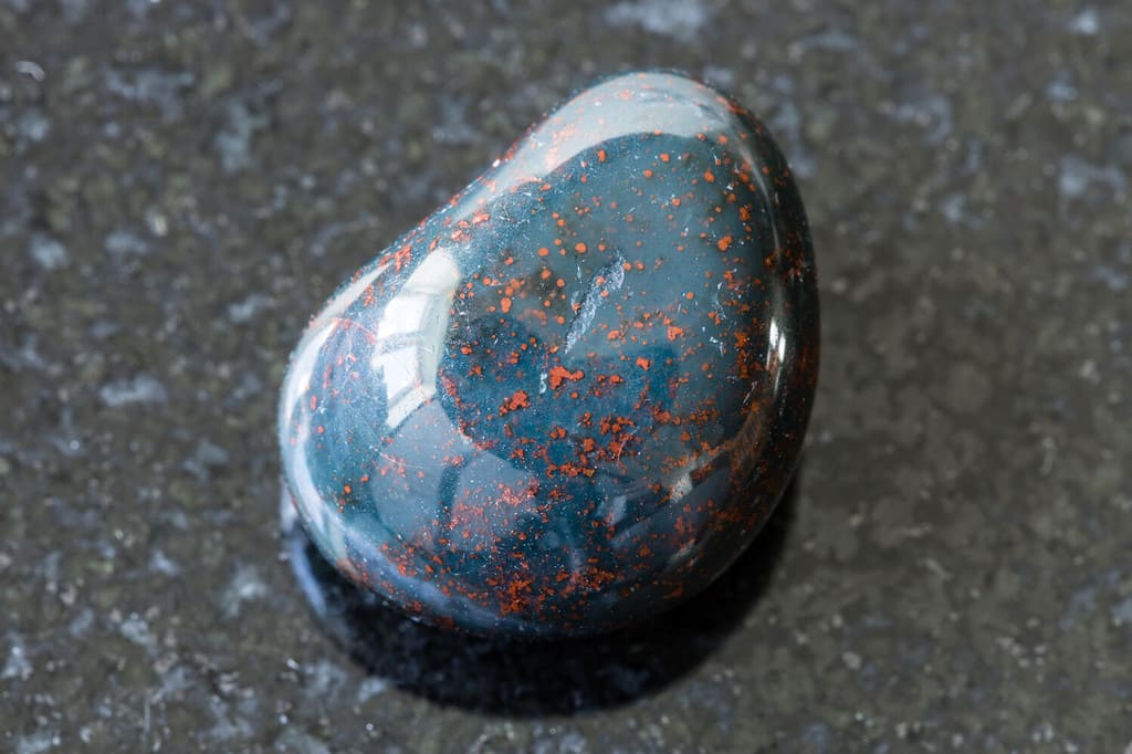 macrofotografia di un campione di minerale naturale proveniente dalla raccolta geologica - pietra preziosa di eliotropio (Bloodstone) burattata su sfondo di granito nero