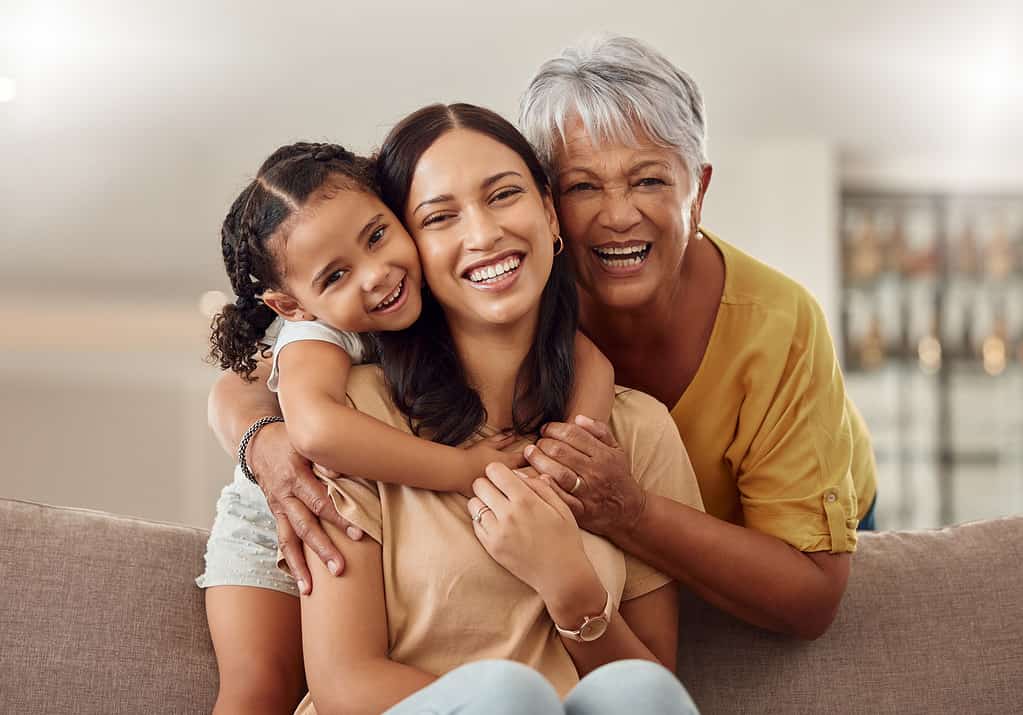 Nonna, mamma e bambino si abbracciano in un ritratto per la festa della mamma sul divano di una casa come una famiglia felice in Colombia.  Sorridi, la mamma e la donna anziana adorano abbracciare una ragazza o un bambino e godersi del tempo di qualità