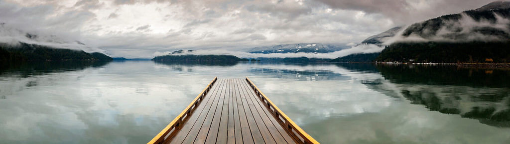 Dock in legno sul lago Harrison, British Columbia, Canada.  Sembra che un molo si stia dirigendo verso il nulla su un lago nel Pacifico nordoccidentale.  Resort delle sorgenti termali di Harrison.