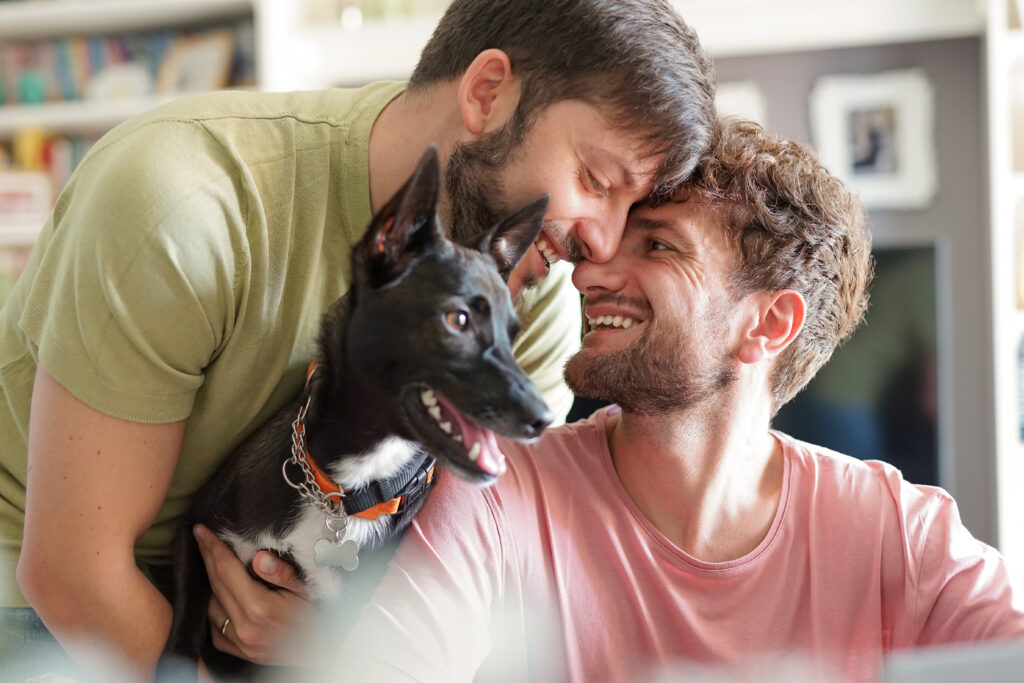 Primo piano di una felice coppia gay con cane adottato al rifugio per animali - Ritratto di giovane con animale domestico mentre bacia suo marito