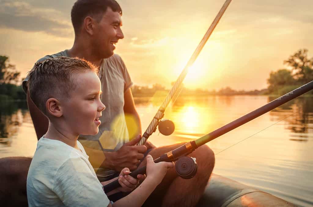 Padre e figlio felici insieme pescano da una barca al tramonto in una giornata estiva sotto un bel cielo sul lago.