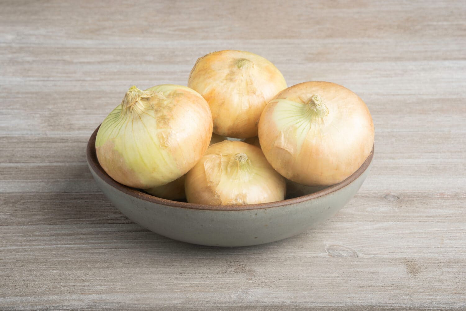 Un mazzo di autentiche cipolle bianche dolci del sud disposte ad arte su una ciotola di ceramica posta su un pannello di legno rustico dipinto di bianco.