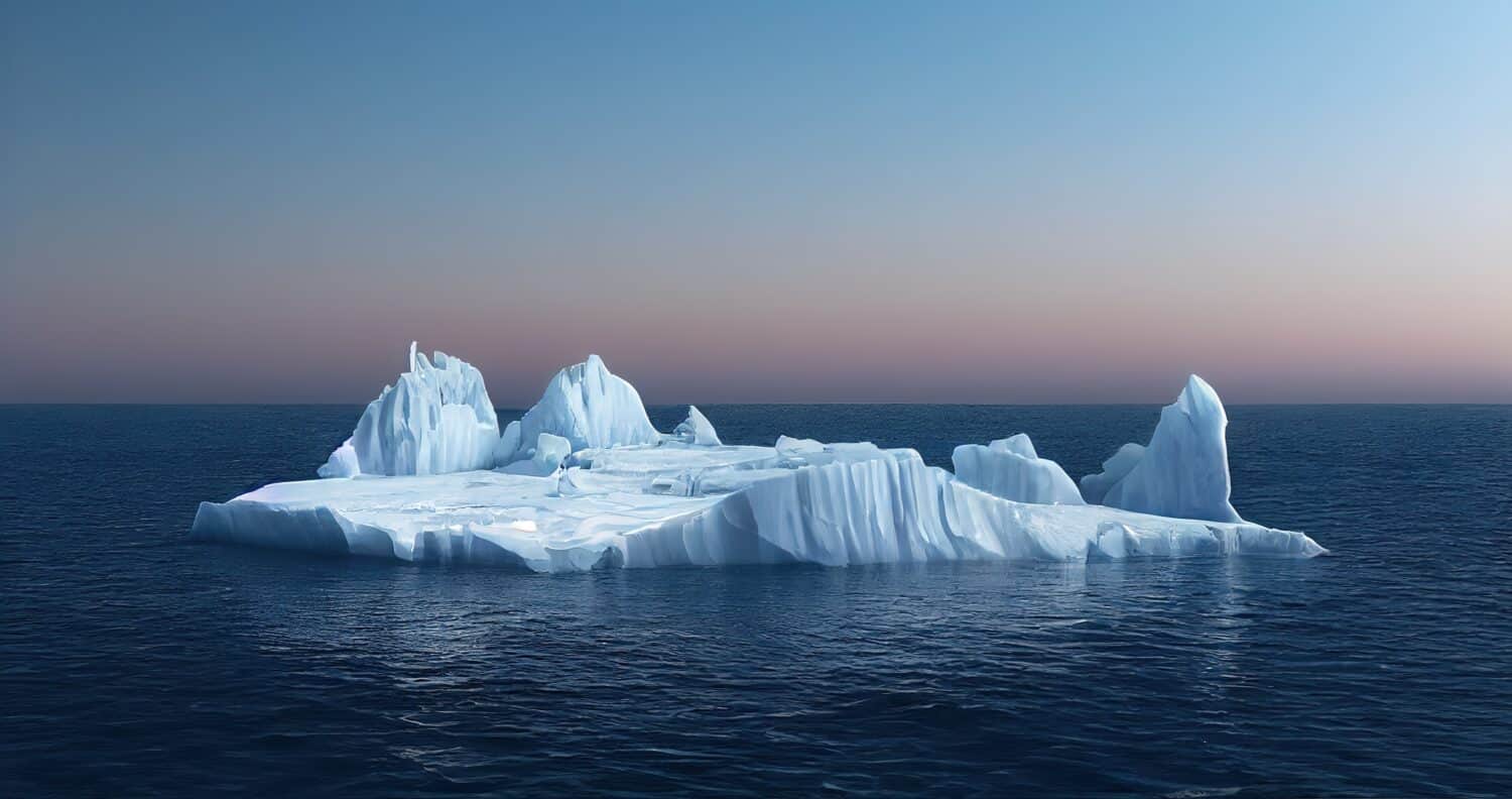 Sulla superficie dell'acqua blu del mare galleggia un'isola di ghiaccio bianca.  Il mare è calmo.  L'acqua è liscia e blu.  Il ghiaccio è limpido e bianco.  Il cielo è limpido