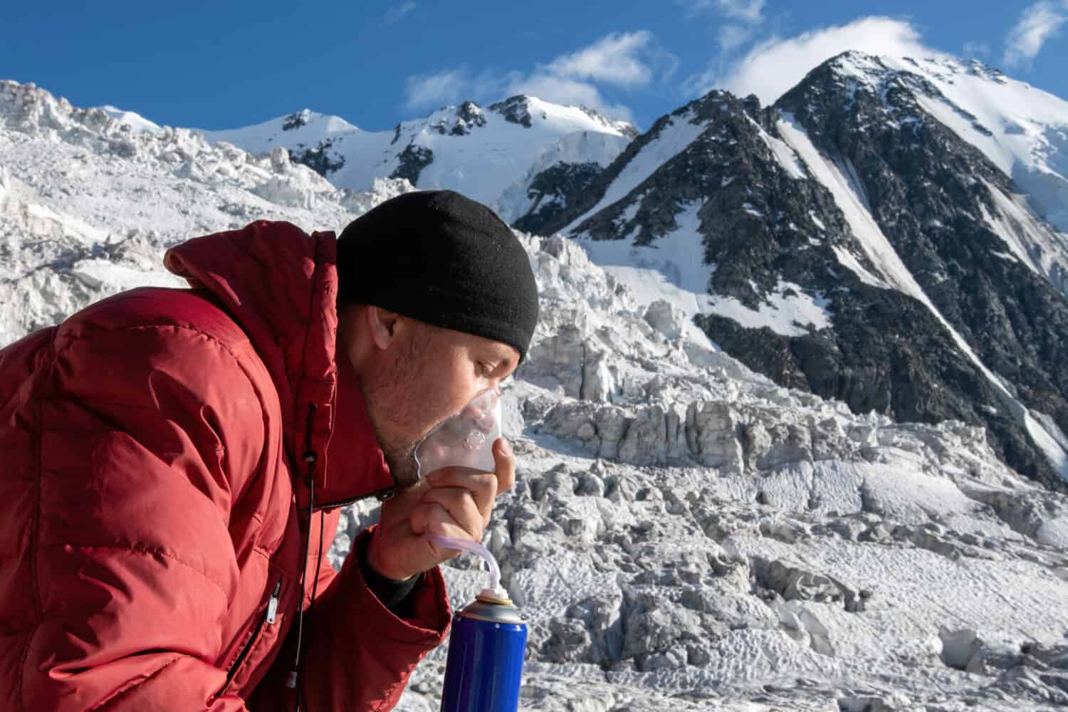 Mal di alta quota.  Scalatore che respira ossigeno dal serbatoio O2 sullo sfondo del ghiacciaio e coperto di montagne di neve e ghiaccio.