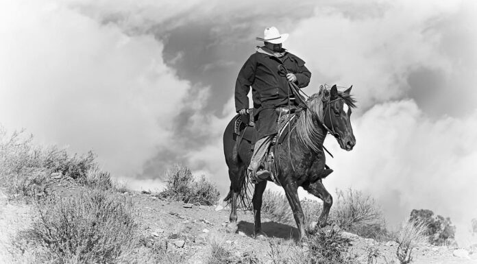 Pony Express Ridge Rider 1 in bianco e nero.  Un cowboy solitario con un cappotto nero cavalca il suo cavallo lungo un crinale montuoso con cieli drammatici dietro di lui.