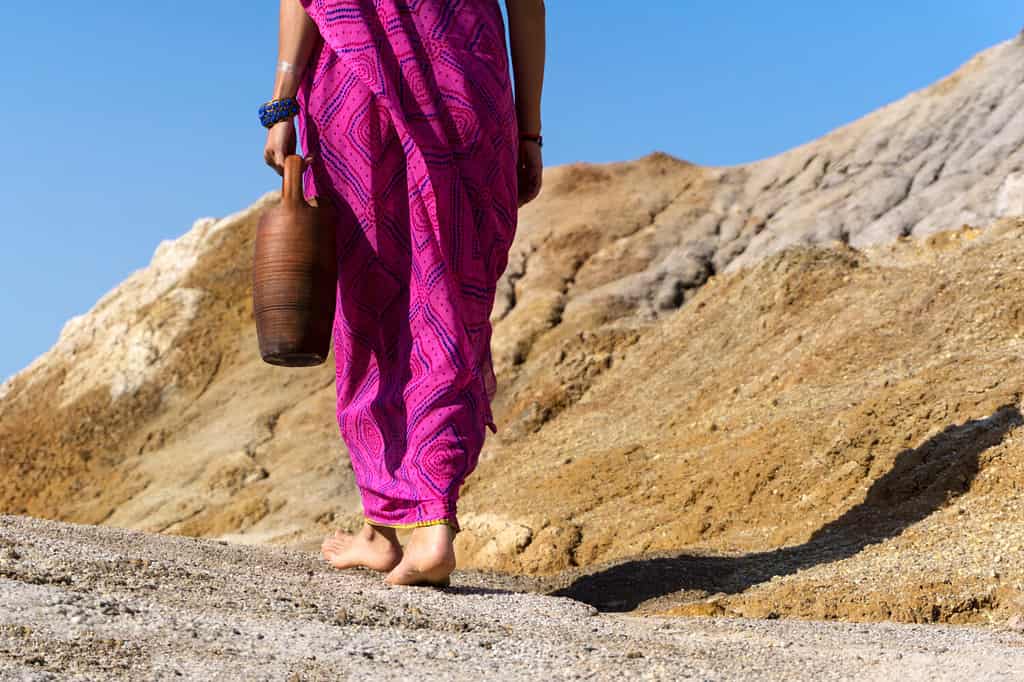 una donna scalza in abiti etnici porta in mano una brocca di terracotta