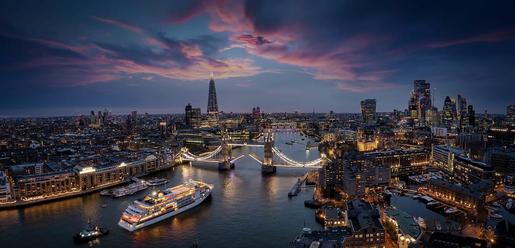 Vista panoramica e aerea dello skyline di Londra con una nave da crociera sfocata in movimento che passa sotto il Tower Bridge sollevato durante il crepuscolo, Inghilterra