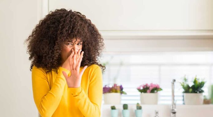 Donna afroamericana che indossa un maglione giallo in cucina che sente l'odore di qualcosa di puzzolente e disgustoso, intollerabile, trattenendo il respiro con le dita sul naso.  Concetto di cattivi odori.