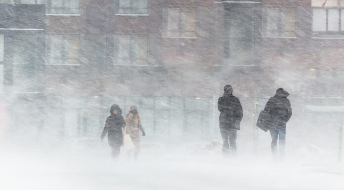 La bufera di neve, il forte vento, il nevischio, sullo sfondo delle case sagome sfocate di persone, cercano di nascondersi dal maltempo, superano tutte le difficoltà del clima rigido.  vai alla fermata dell'autobus.