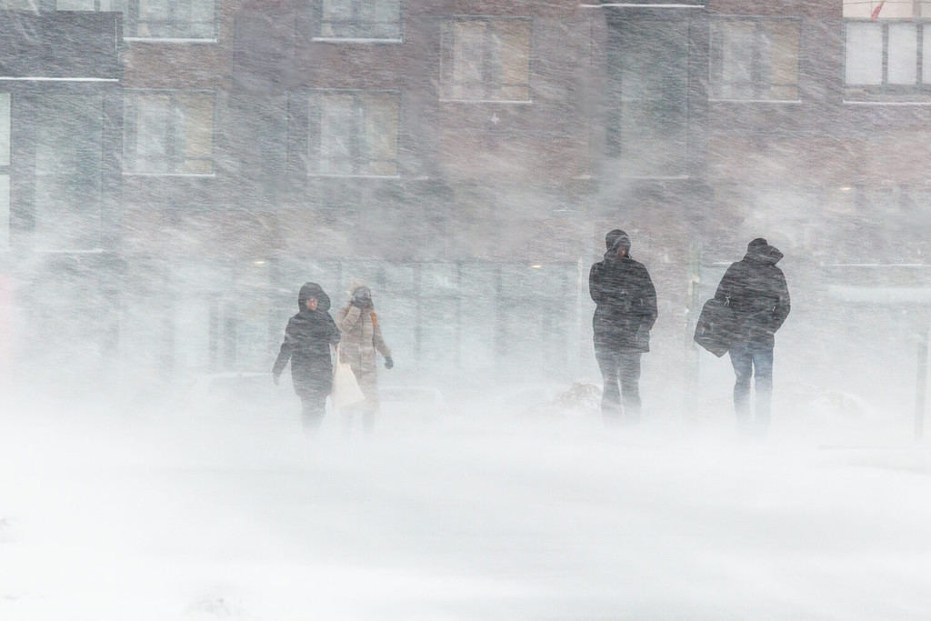 La bufera di neve, il forte vento, il nevischio, sullo sfondo delle case sagome sfocate di persone, cercano di nascondersi dal maltempo, superano tutte le difficoltà del clima rigido.  vai alla fermata dell'autobus.