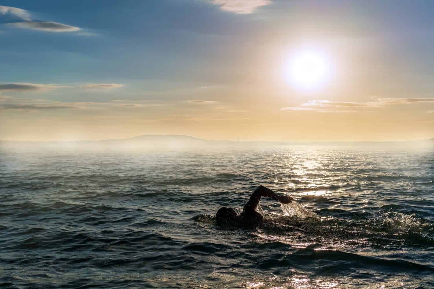 Uomo che nuota in acque aperte durante un tramonto nebbioso