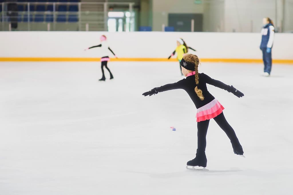 Bambina che impara a pattinare sul ghiaccio.  Scuola di pattinaggio artistico.  Giovane pattinatore che pratica sulla pista di pattinaggio al coperto.