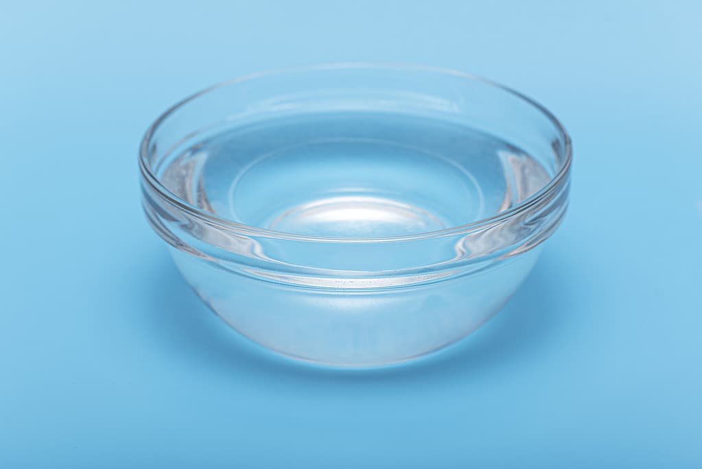 Acqua potabile pura e limpida in una ciotola o piatto di vetro su sfondo blu