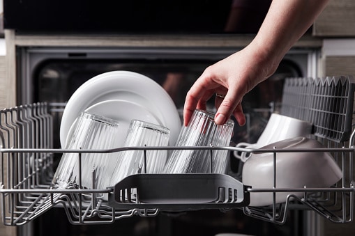 Lavastoviglie aperta con posate, bicchieri e piatti puliti all'interno della cucina di casa