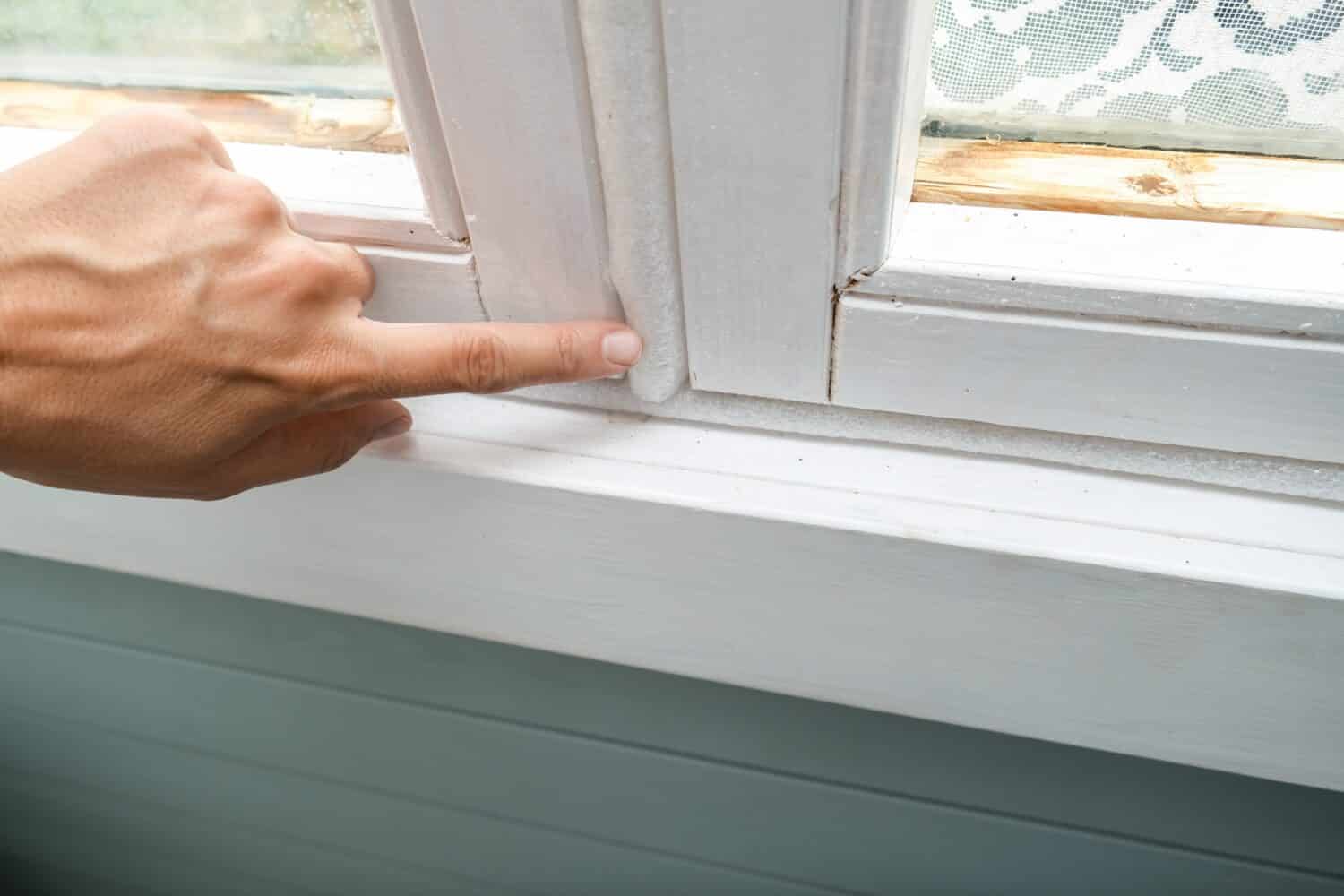 Mano della donna che isola le vecchie finestre per evitare perdite di calore e correnti d'aria, preparando la casa per l'inverno e il freddo