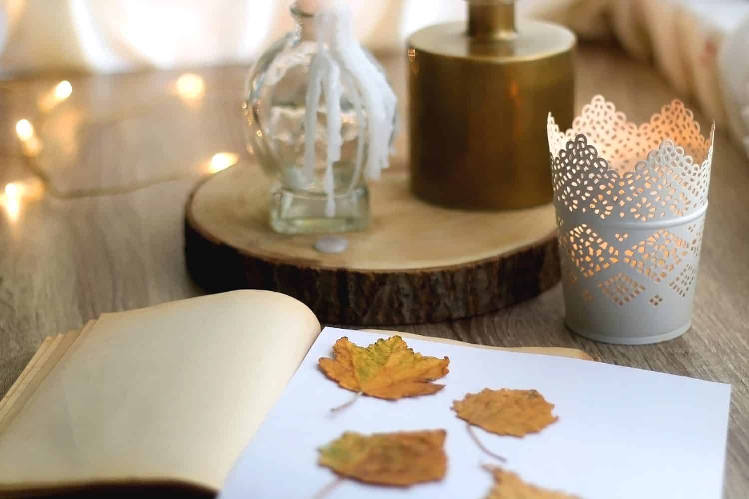 Vecchio libro con foglie autunnali pressate, candele accese e vaso con fiori di gypsophila.  Messa a fuoco selettiva.