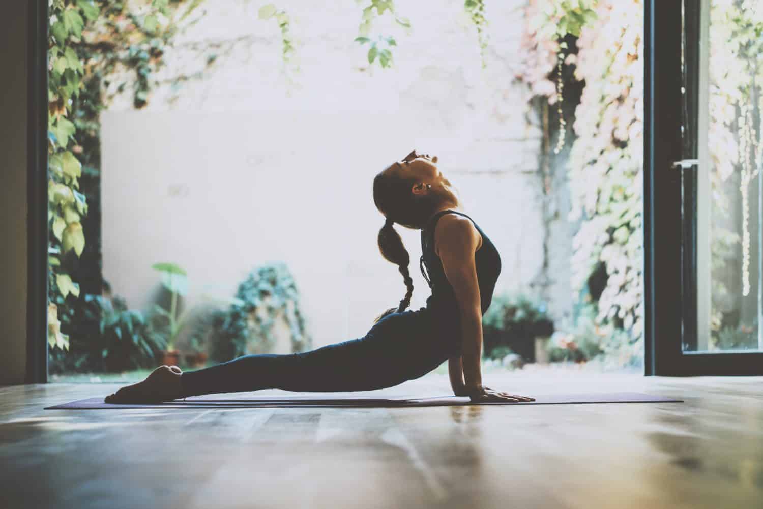 Ritratto di giovane donna splendida che pratica yoga al coperto.  Bella ragazza pratica cobra asana in classe. Calma e relax, felicità femminile. Sfondo orizzontale e sfocato