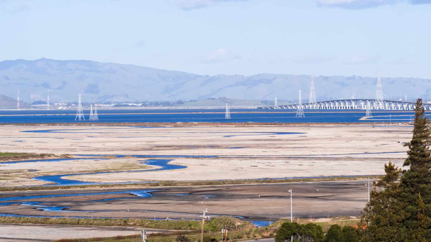 Sale che si accumula sugli stagni poco profondi della baia di San Francisco con la bassa marea, torri elettriche e ponte Dumbarton sullo sfondo, California