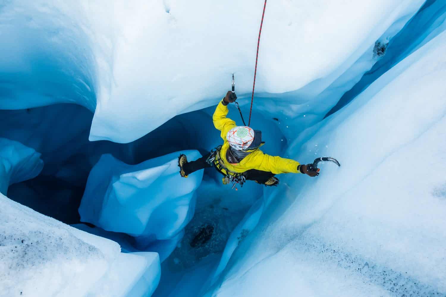 Lo scalatore di ghiaccio scende da un pilastro indipendente all'interno di una grotta di ghiaccio mentre esce dalla cima della grotta.
