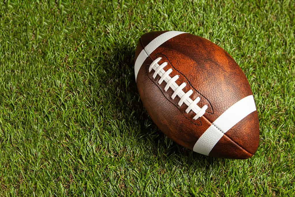 Palla di football americano sul fondo del campo di erba verde.