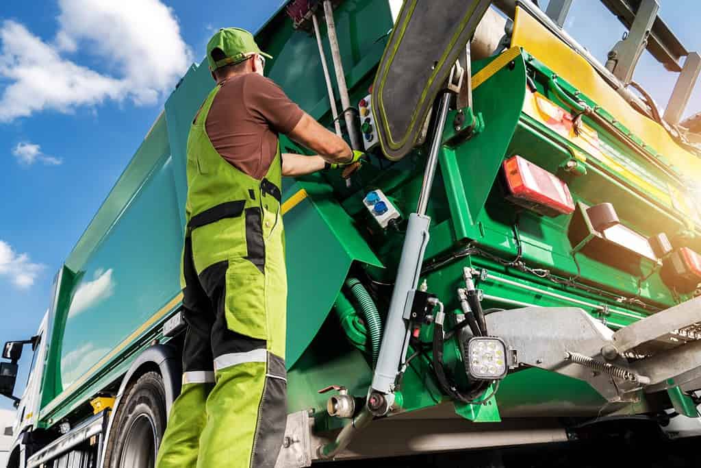 Moderno camion della spazzatura e lavoratore caucasico del raccoglitore di rifiuti.  Tema sulla raccolta differenziata e sulla gestione dei rifiuti.