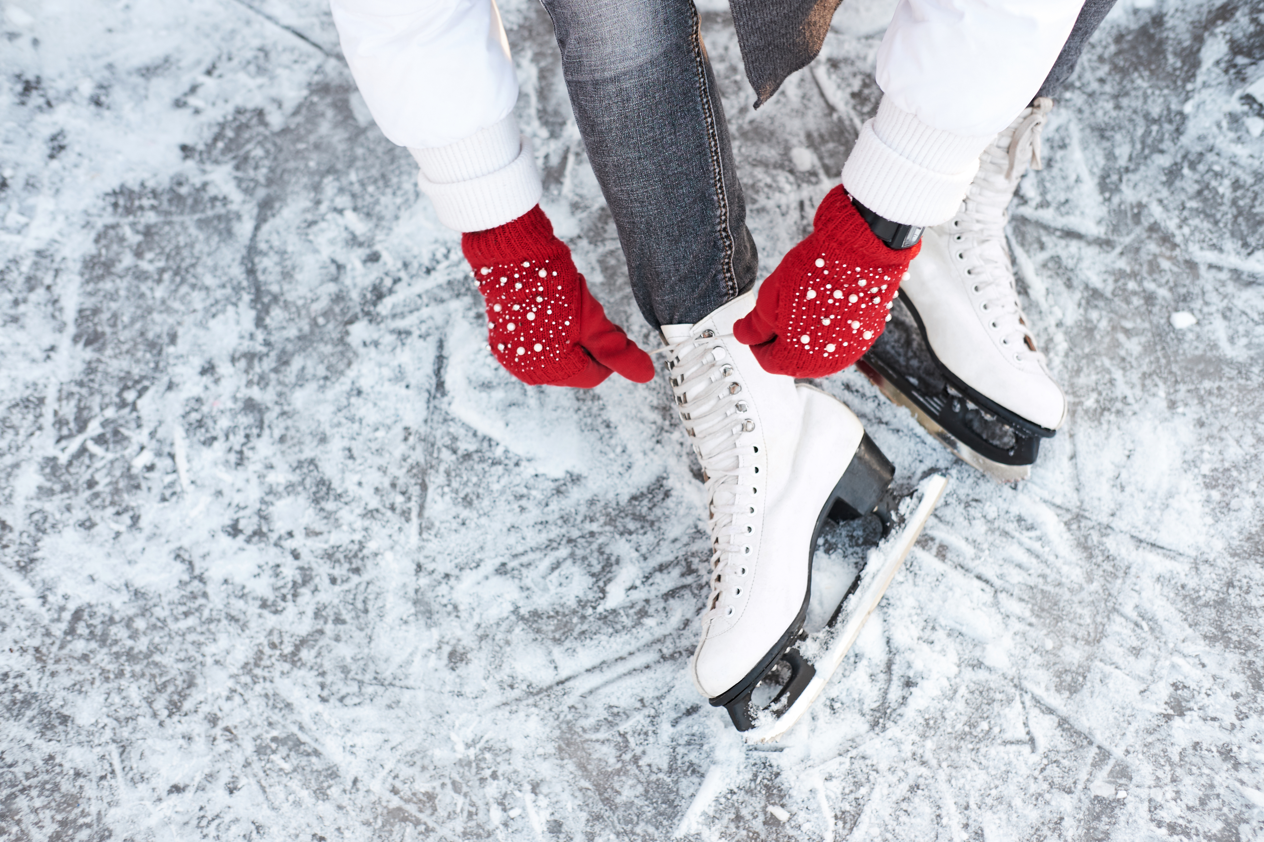 Ragazza che allaccia i lacci delle scarpe sui pattini da ghiaccio prima di pattinare sulla pista di pattinaggio, mani con guanti a maglia rossi.