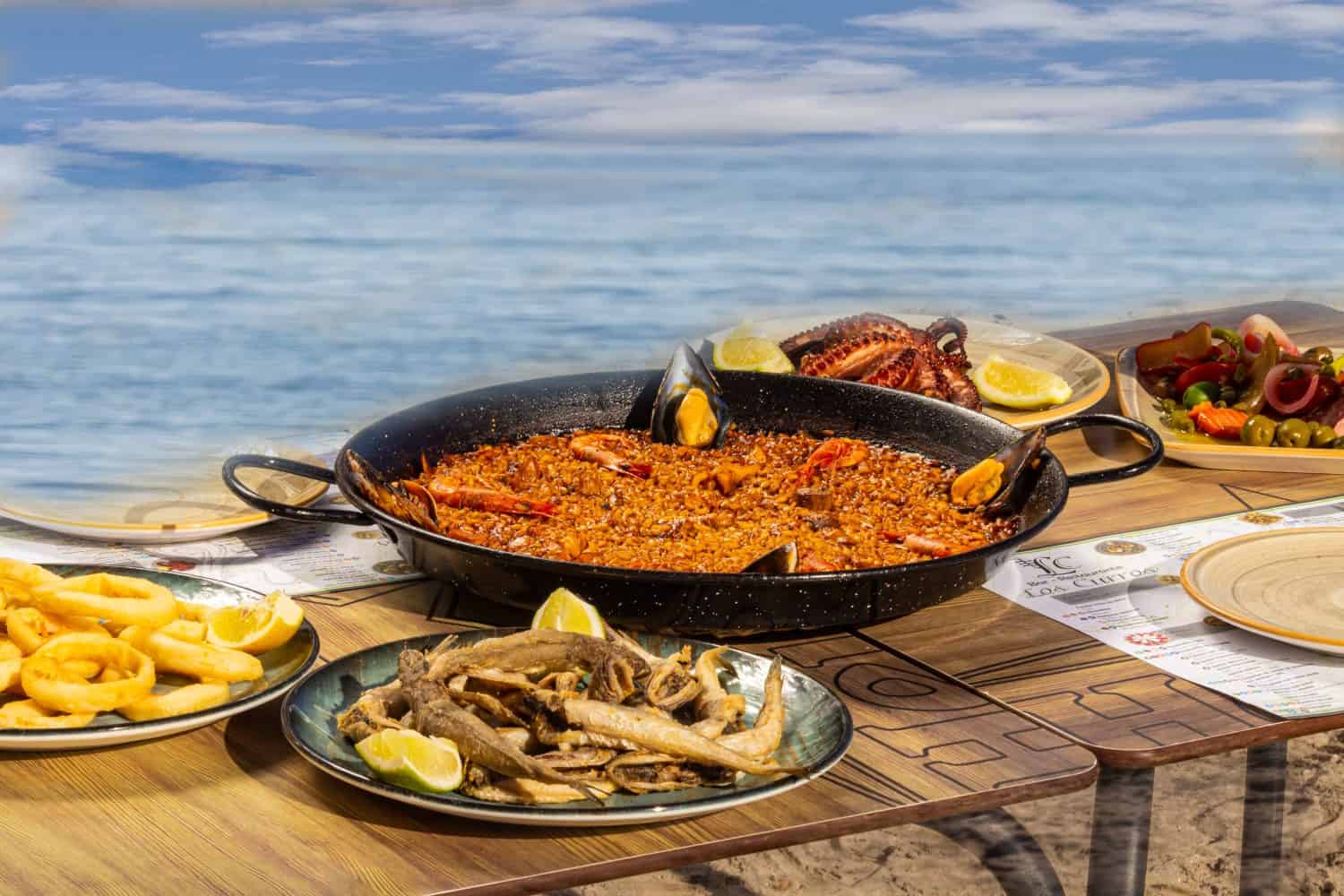 Paella, piatto nazionale spagnolo, con frutti di mare in una padella speciale sullo sfondo del mare in un ristorante sulla spiaggia.