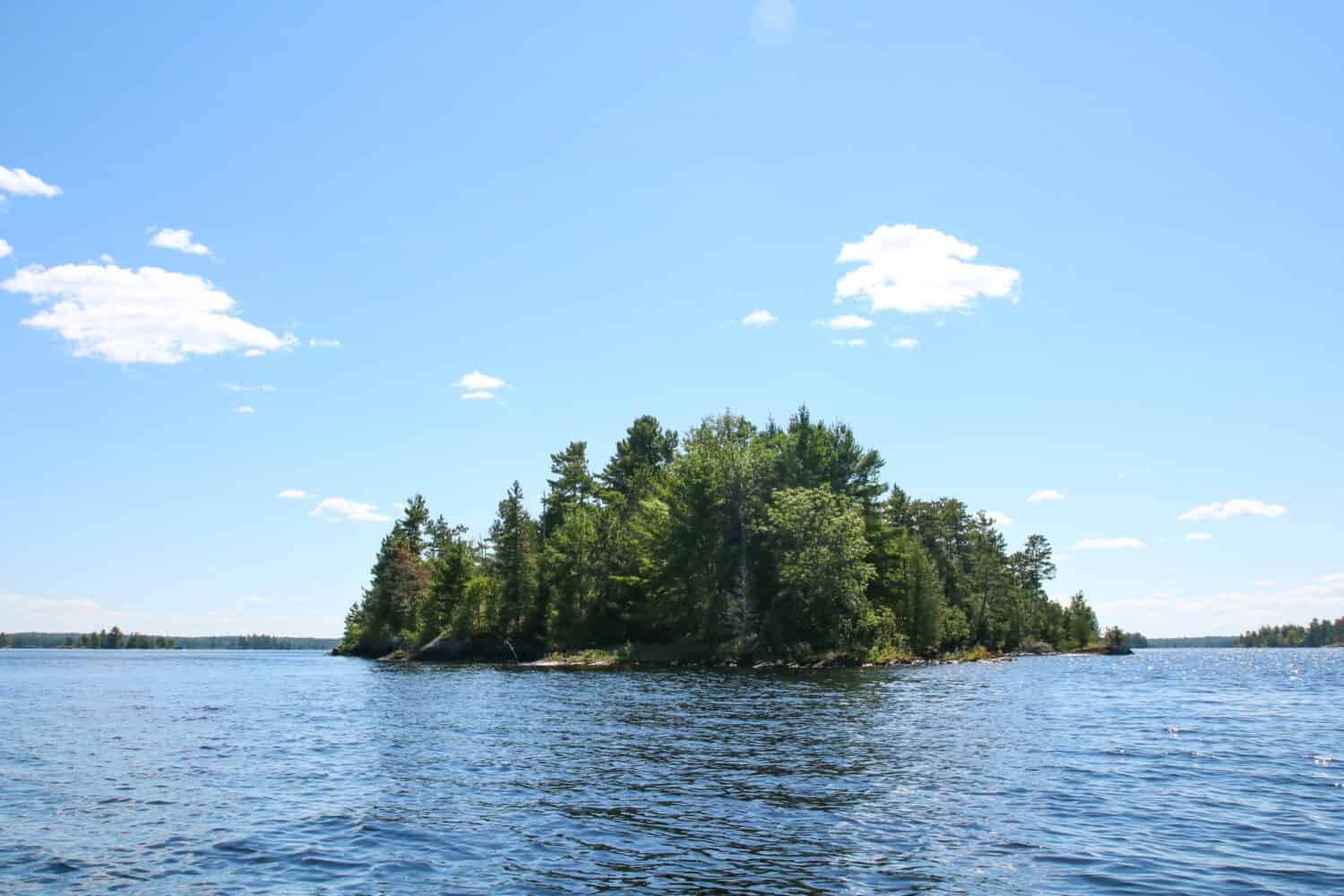 Una piccola isola su Rainy Lake, Minnesota, situata a International Falls.  Il lago e il cielo sono blu con poche nuvole bianche.  Il lago si trova nel Parco Nazionale Voyageur.