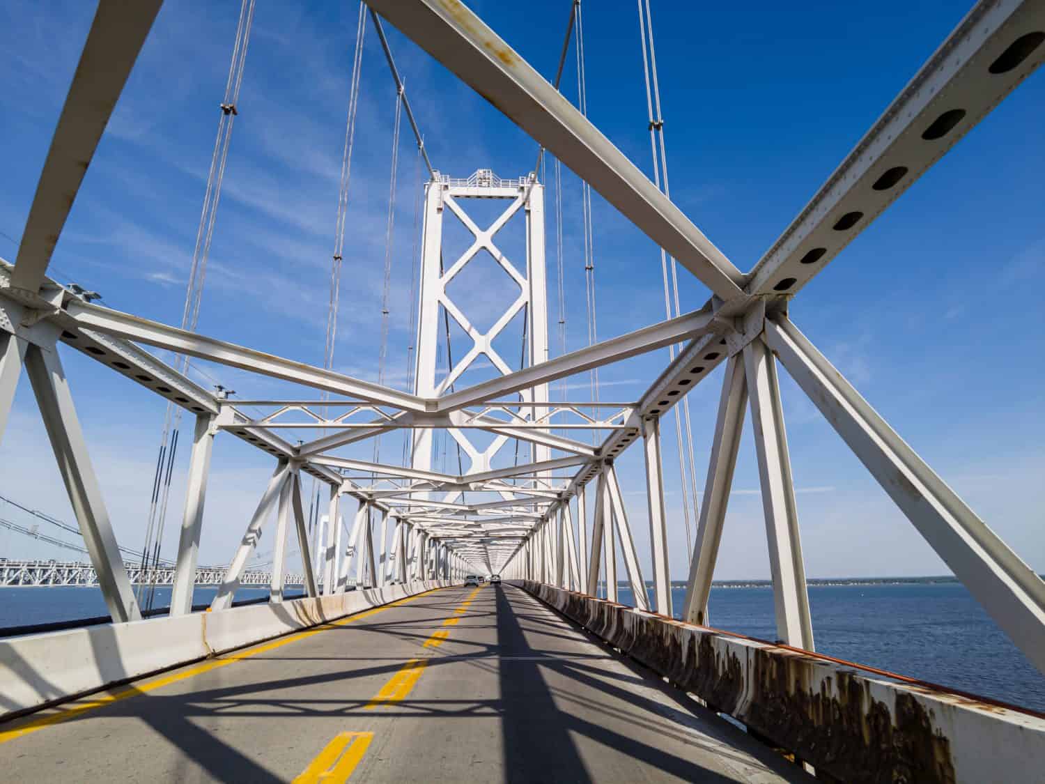 Immagine che mostra l'attraversamento del famoso ponte di Chesapeake Bay (William Preston Lane Jr. Memorial Bridge) sotto le travi di sospensione di piloni in stile traliccio metallico.  Si vedono le torri sull'altro lato.
