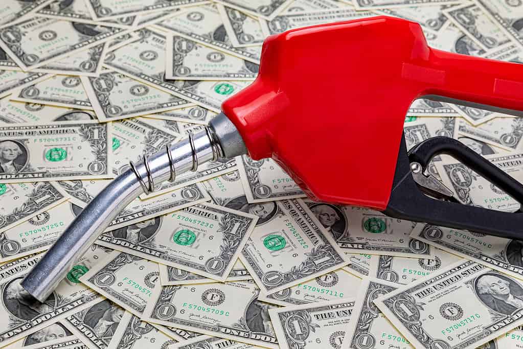 Ugello del carburante della benzina e denaro contante.  Concetto di prezzo del gas, tasse, etanolo e combustibili fossili