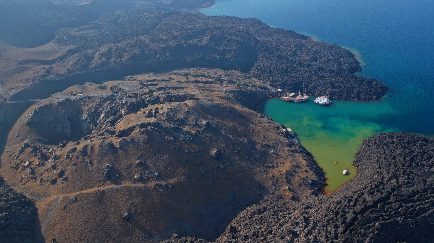 Foto aerea del drone dell'iconico cratere principale dell'isola vulcanica di Santorini chiamata Kameni visitata da imbarcazioni turistiche, Cicladi, Grecia