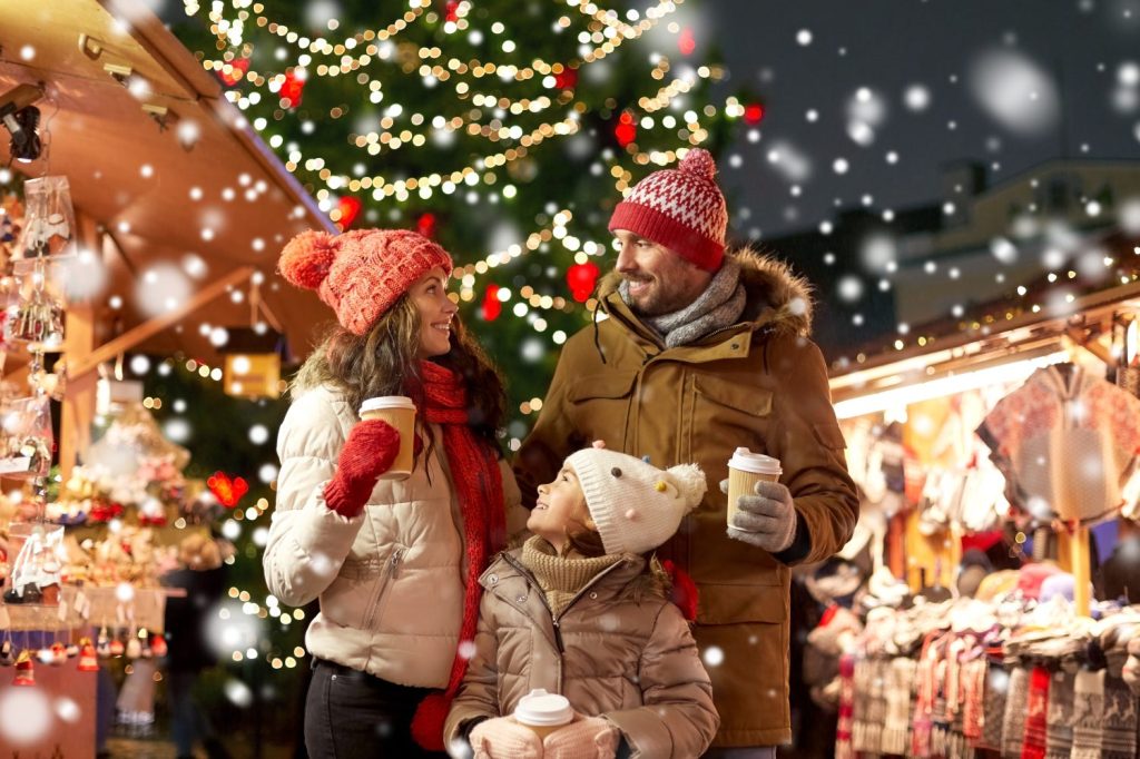 concetto di famiglia, vacanze invernali e celebrazione - madre, padre e figlia felici con bevande da asporto al mercatino di Natale sulla piazza del municipio a tallinn, in estonia, sulla neve