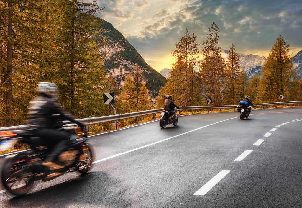 Concetto di viaggio.  Gruppo di persone che viaggiano in motocicletta su una strada asfaltata in montagna al tramonto nelle Alpi italiane Bellissimo paesaggio autunnale