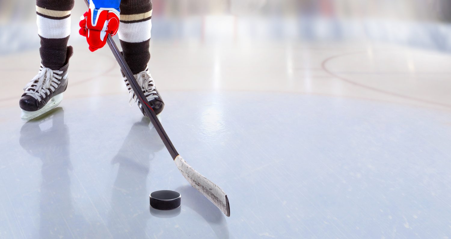 Vista ad angolo basso del giocatore di hockey su ghiaccio con il bastone sulla pista di pattinaggio sul ghiaccio che controlla il disco e lo spazio della copia.