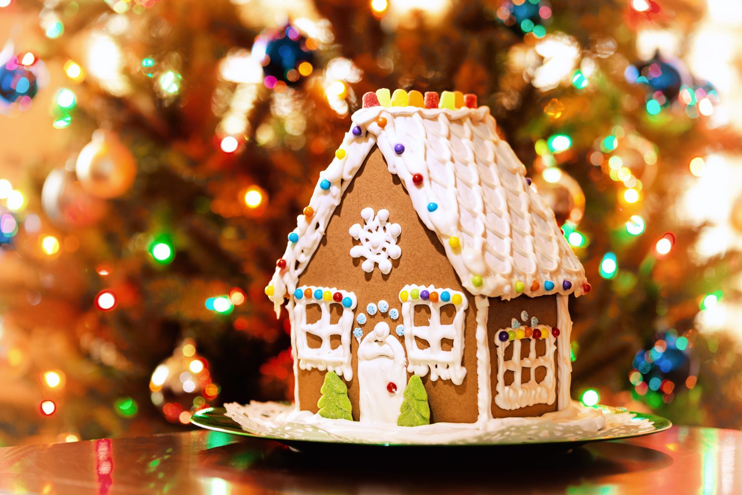 Casa di pan di zenzero di Natale fatta in casa esposta su un tavolo.  Sullo sfondo le luci dell'albero di Natale.