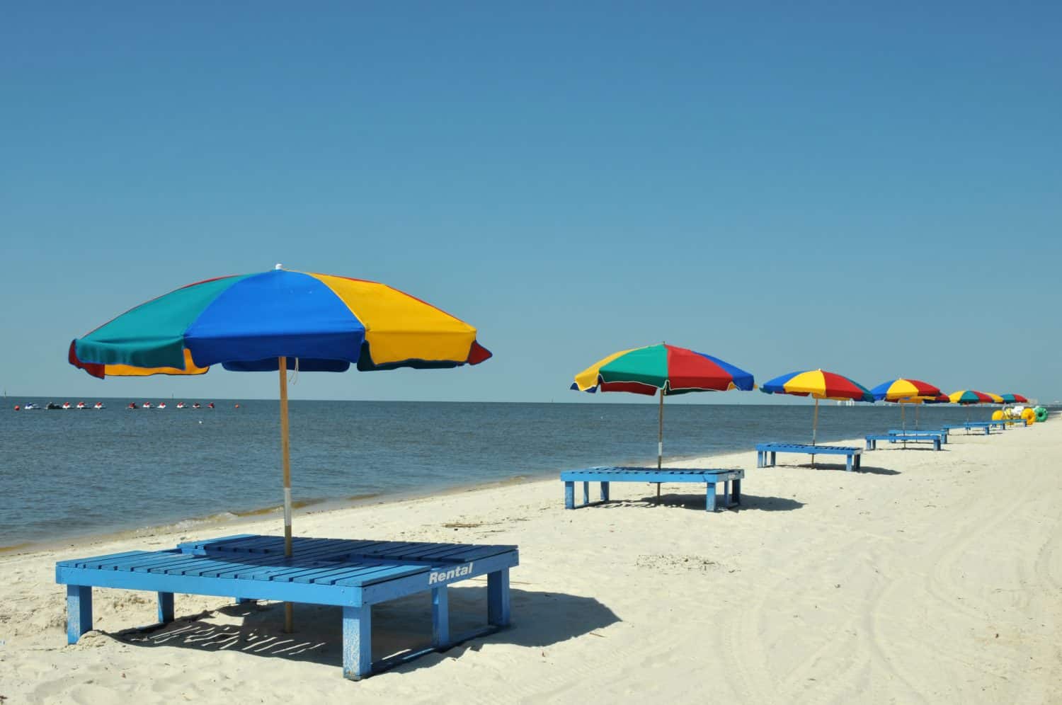 Sedie a sdraio, ombrelloni e trike di grandi dimensioni sparsi lungo la spiaggia di Biloxi nel Mississippi in una giornata primaverile.