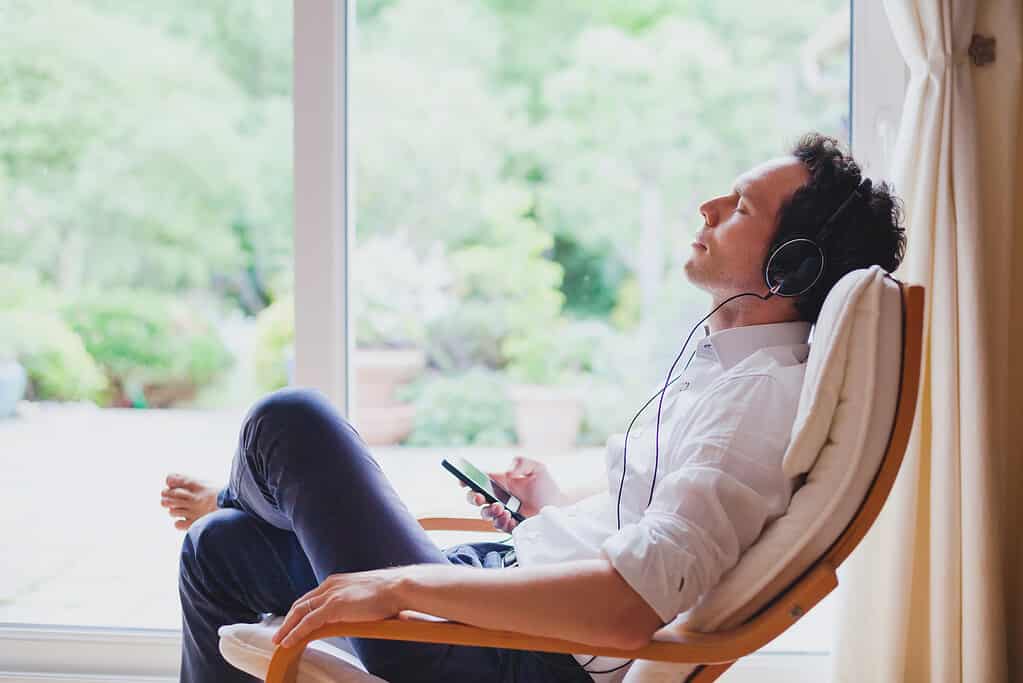 Ascolta musica rilassante a casa, uomo rilassato seduto in cuffia.