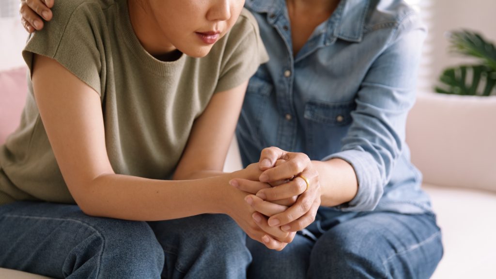 Persone di mezza età asiatiche, mamma anziana che si tiene per mano, si fidano del comfort e aiutano la giovane donna a parlare piangendo per alleviare lo stress a casa.  La mamma come amica ama la cura, tiene la mano, il bambino adulto sente dolore, triste preoccupazione per i problemi di crisi della vita.