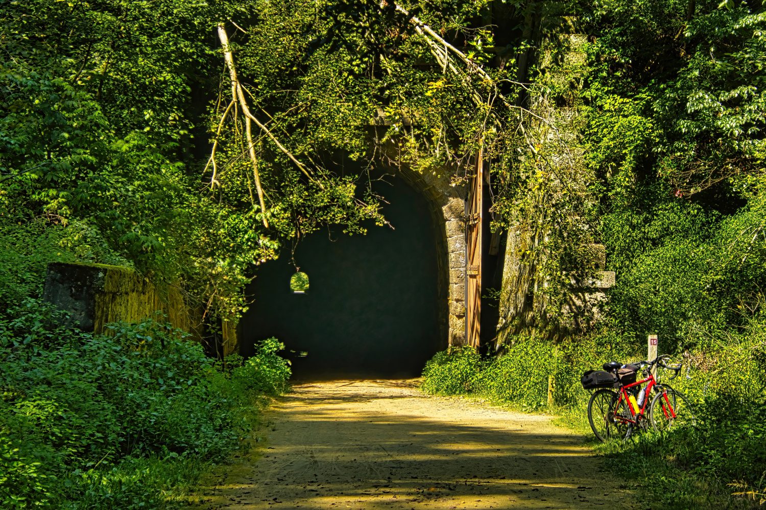 In una soleggiata giornata estiva, una bicicletta rossa poggia contro un indicatore di chilometraggio all'ingresso di uno dei tre tunnel sull'Elroy-Sparta State Trail.