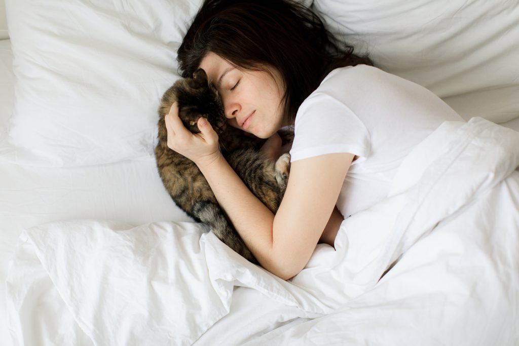 concetto di animali domestici, mattina, comfort, riposo e persone - giovane donna felice con gatto a letto a casa