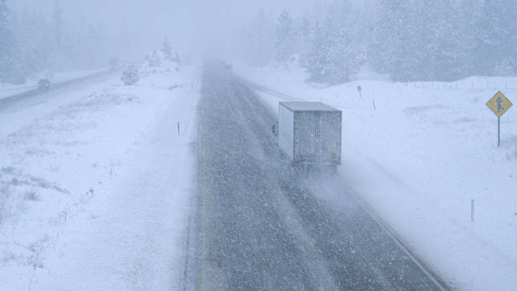 Camion e automobili si fanno strada in una bufera di neve lungo una pericolosa strada di campagna