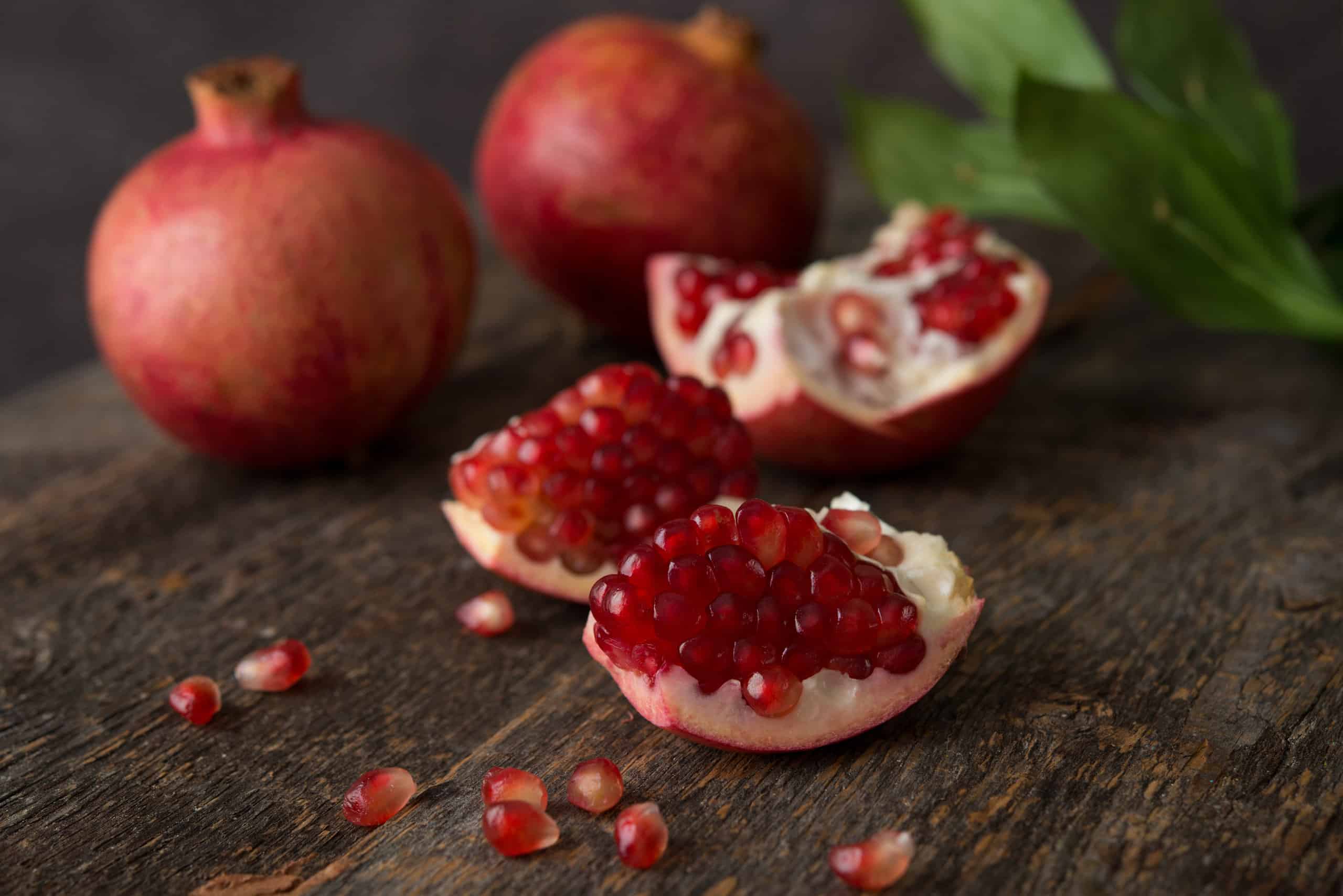 melograno aperto con frutti esposti da due melograni interi non aperti su un tavolo di legno