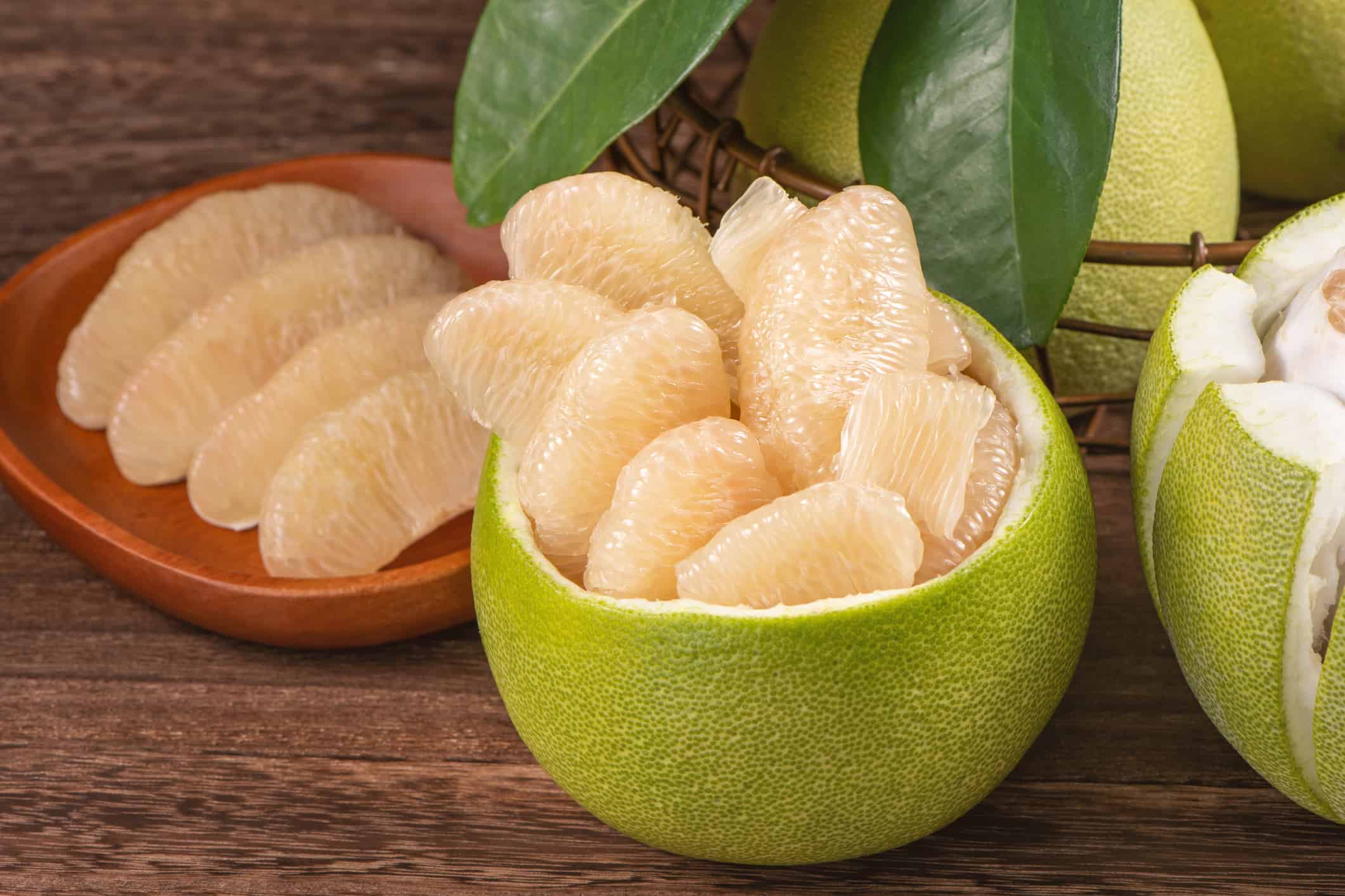 Pomelo fresco sbucciato, pompelmo, shaddock con foglie verdi su tavola di legno scuro.  Frutta di stagione in prossimità della festa di metà autunno.