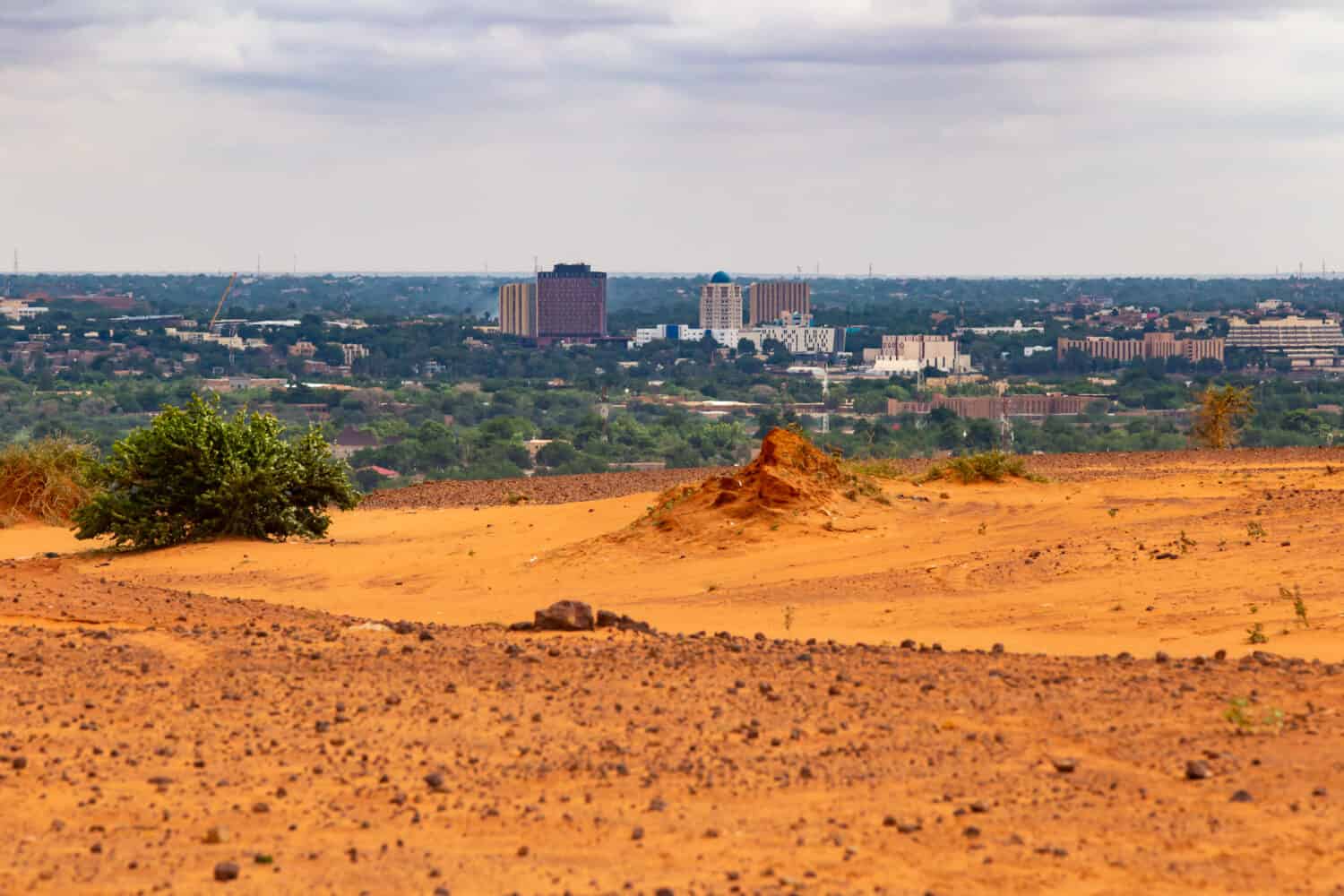 Skyline di Niamey, capitale del Niger, visto da un altopiano secco del Sahel più alto con un cespuglio verde e un termitaio in primo piano parzialmente distrutto dalle piogge nella stagione umida estiva
