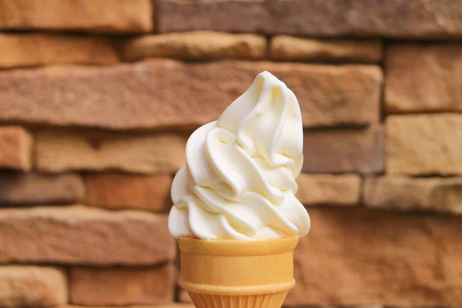 Delizioso cono gelato alla vaniglia con servizio morbido e parete bloccata in pietra sfocata sullo sfondo