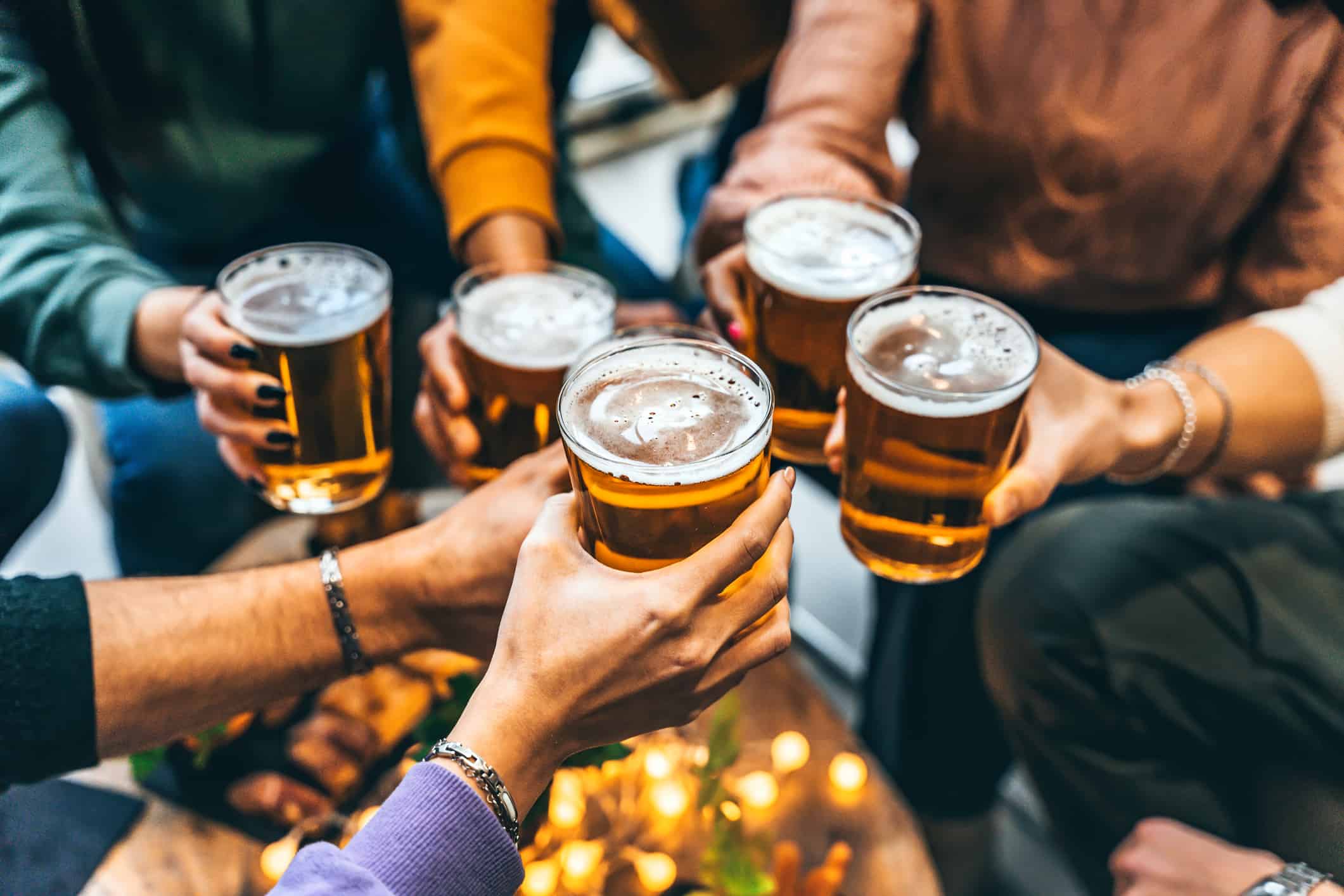 Gruppo di amici che bevono e brindano con un bicchiere di birra al ristorante pub birreria - Persone multirazziali felici che si godono l'happy hour con una pinta seduti al tavolo del bar - Concetto di stile di vita di cibi e bevande per giovani