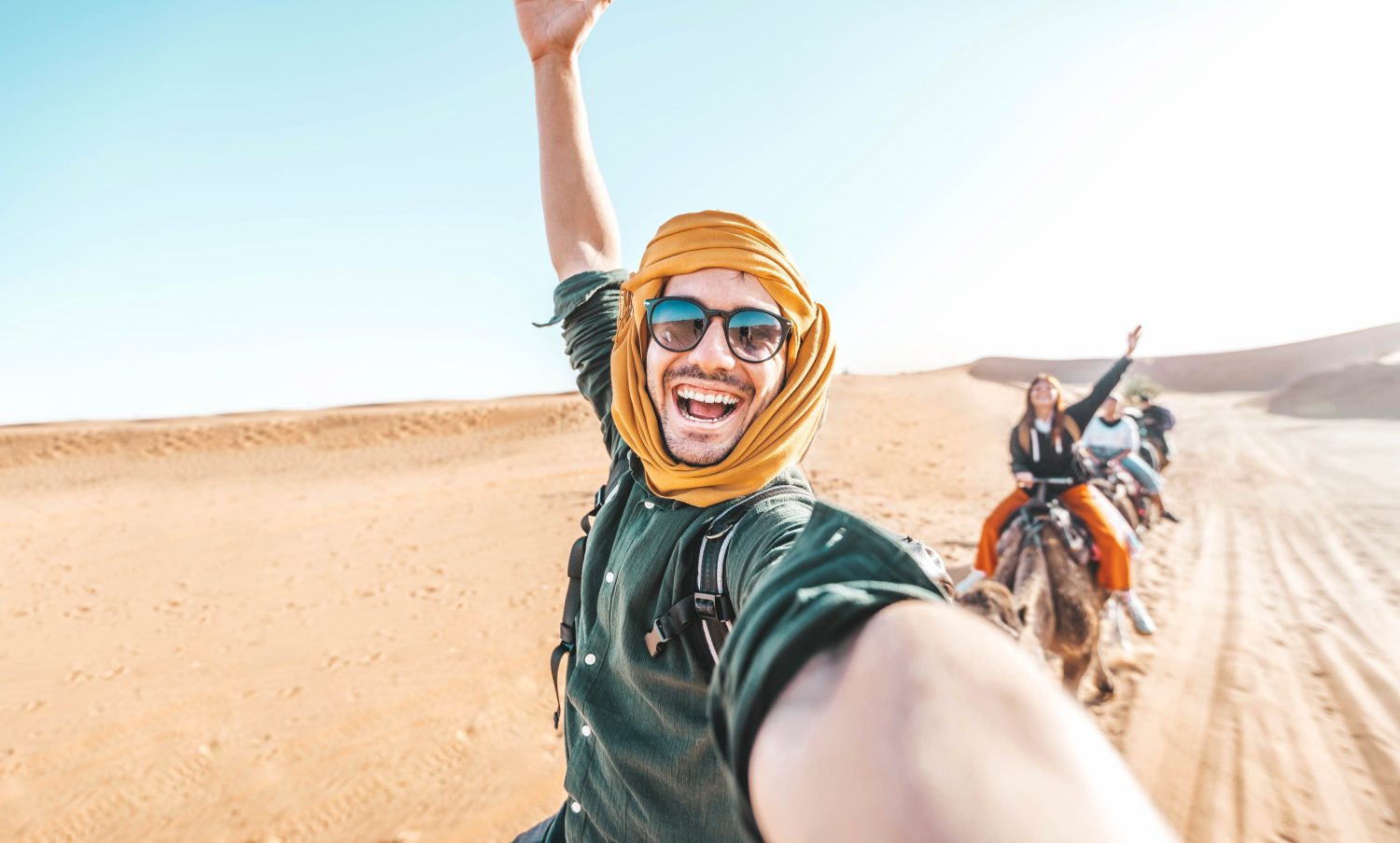 Turista felice che si diverte godendosi un tour di gruppo in cammello nel deserto - Viaggi, stile di vita, attività di vacanza e concetto di avventura