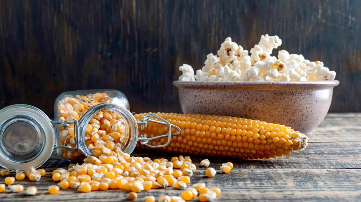 Chicchi di mais crudi versati da un barattolo su un tavolo di legno.  Il concetto di preparare popcorn a casa.