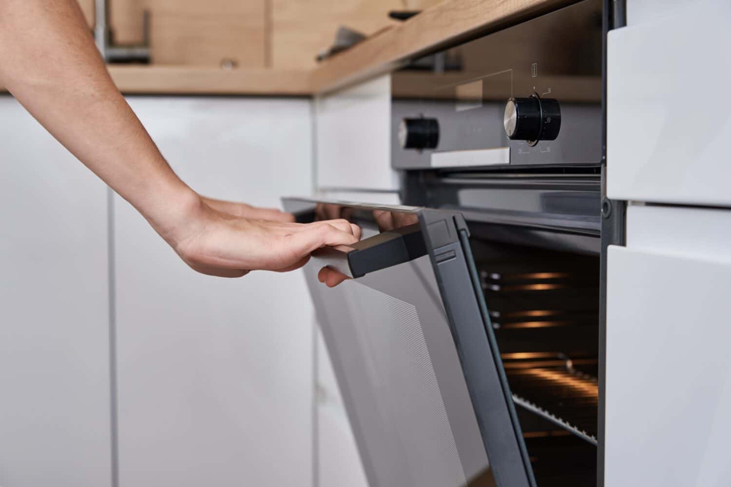 Porta del forno elettrico aperta a mano da donna con maniglia.  Cucina casalinga.  Elettrodomestico da cucina